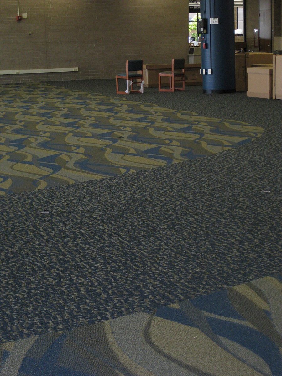 Commercial carpet with curving patterned sections set into a plain blue field in a large open room