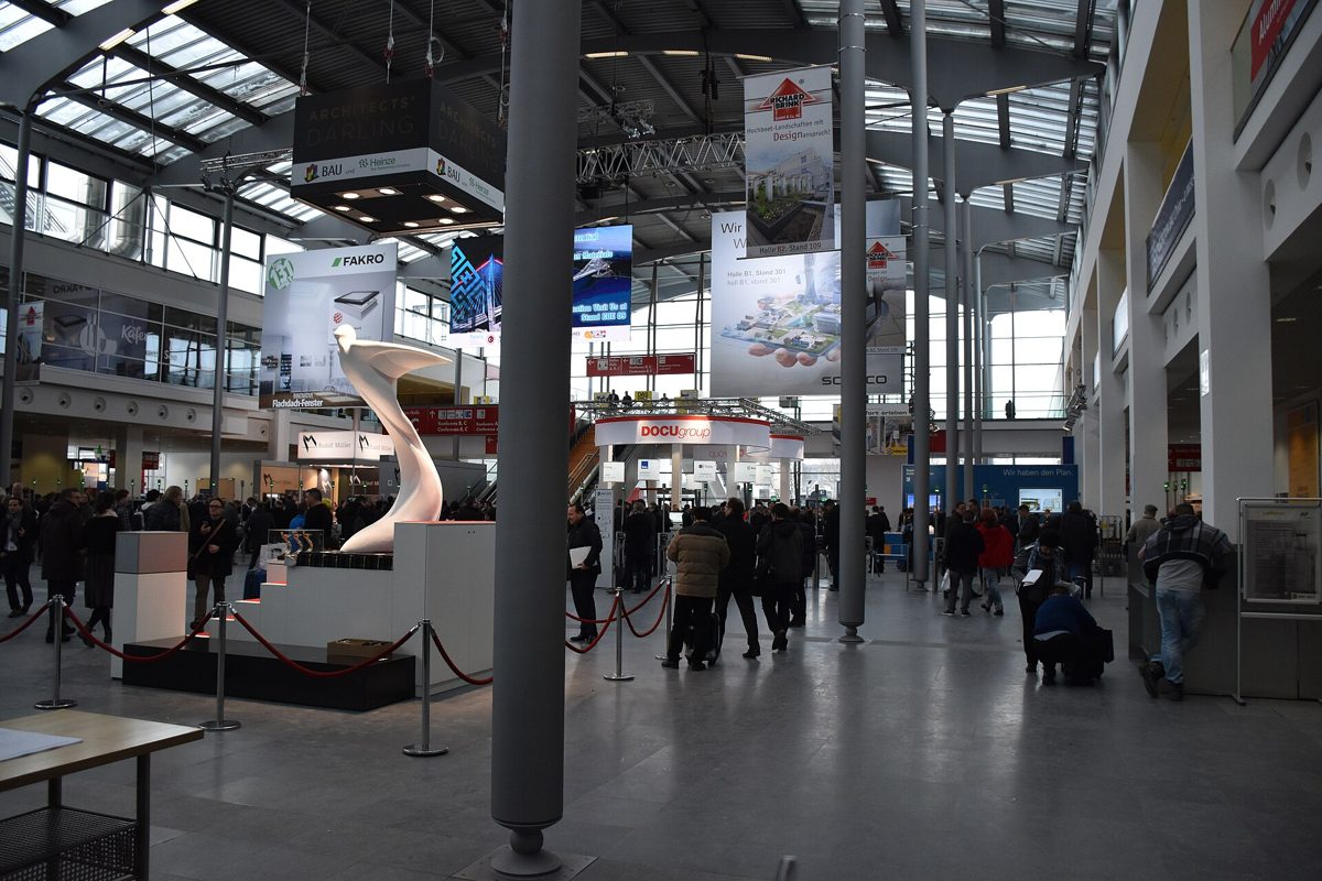 Visitors crossing the main concourse of the BAU building-materials fair in Munich, under hanging exhibitor banners