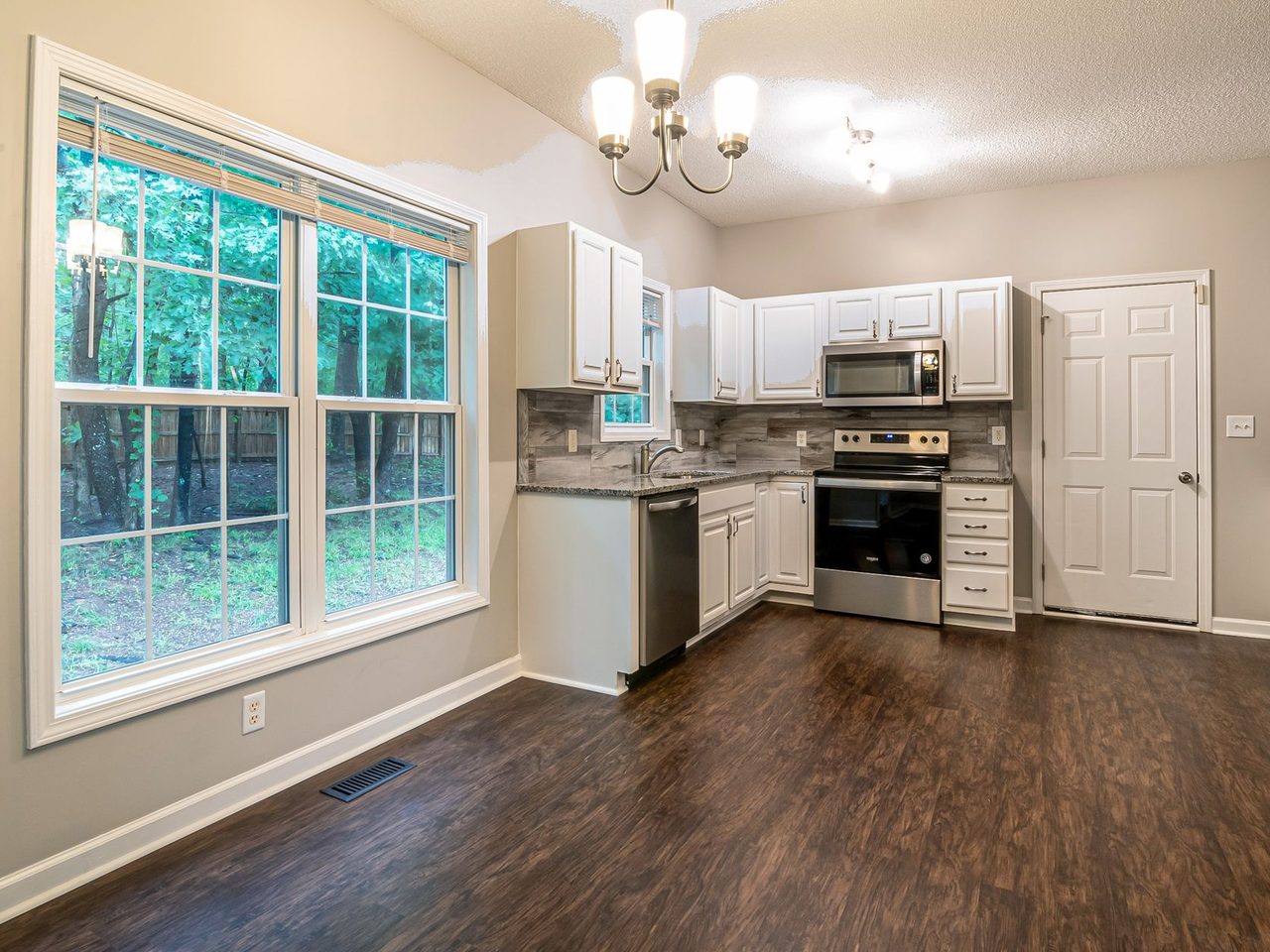 Kitchen with white cabinets, large windows and a dark plank floor