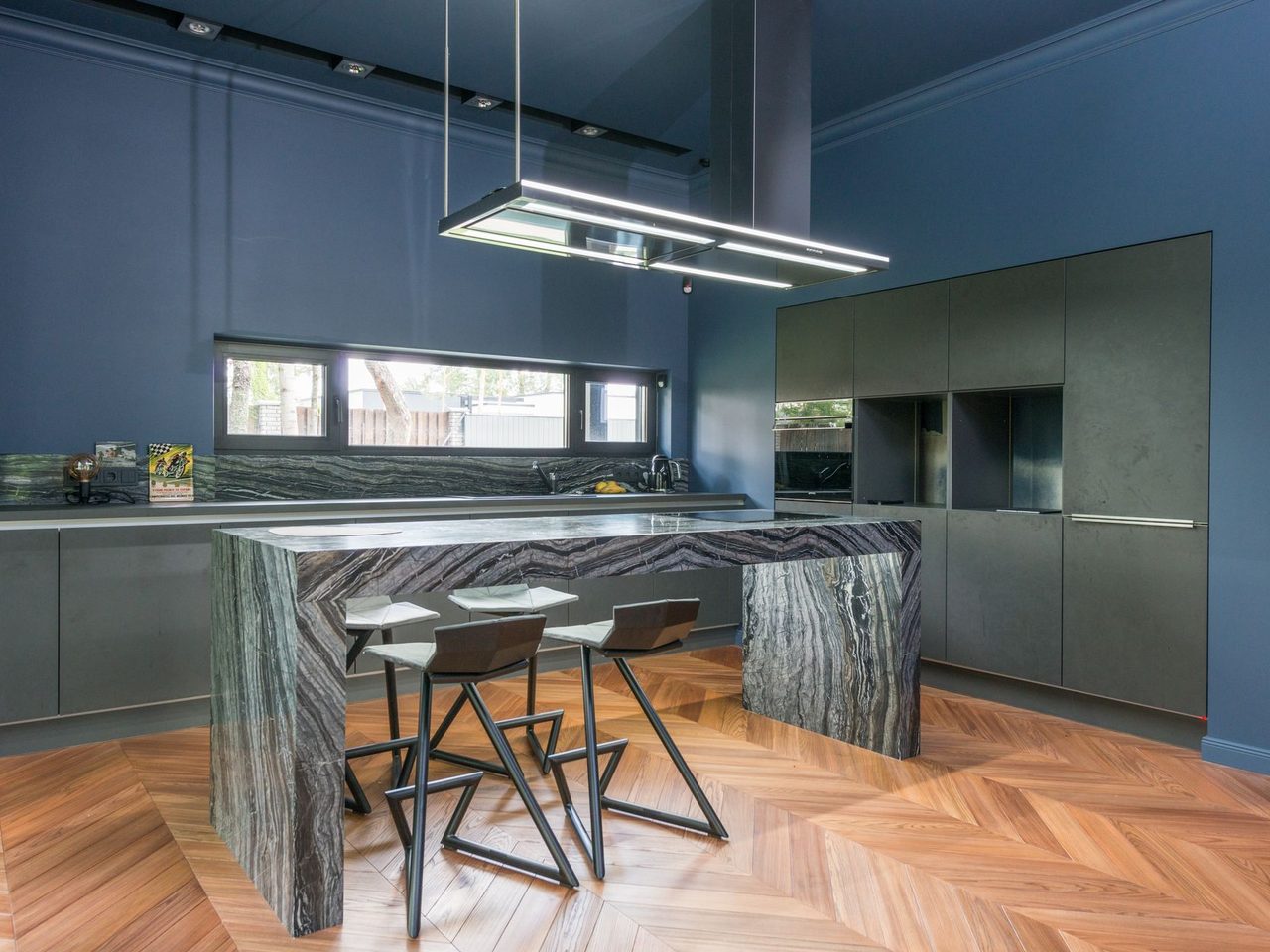 Blue kitchen with a stone island on a herringbone wood-look floor