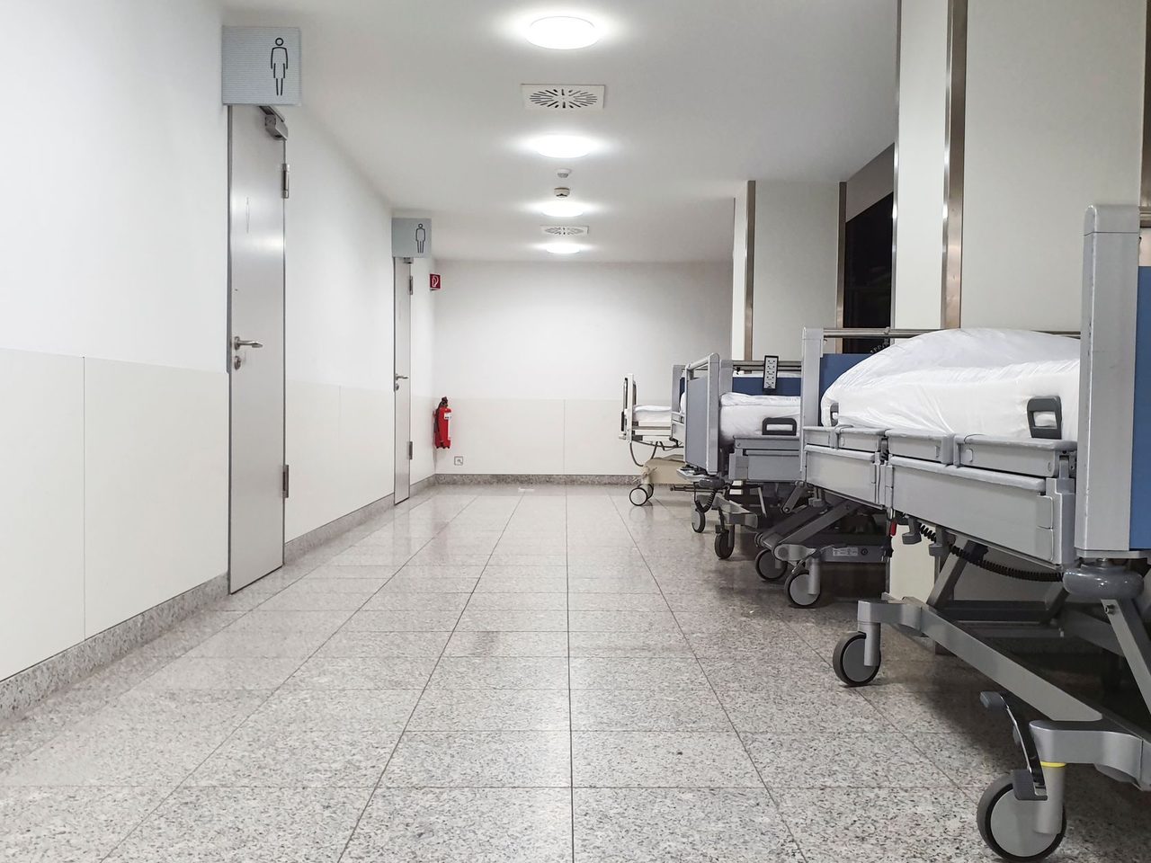 Hospital corridor with empty beds along the wall and a light floor