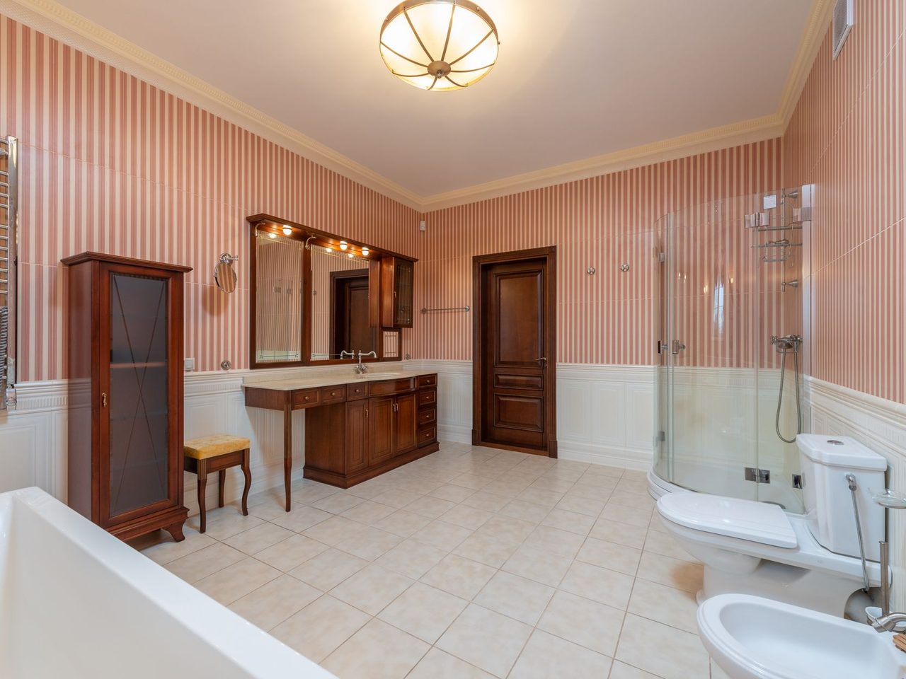 Bathroom with striped wallpaper, wood furniture and a light tile floor