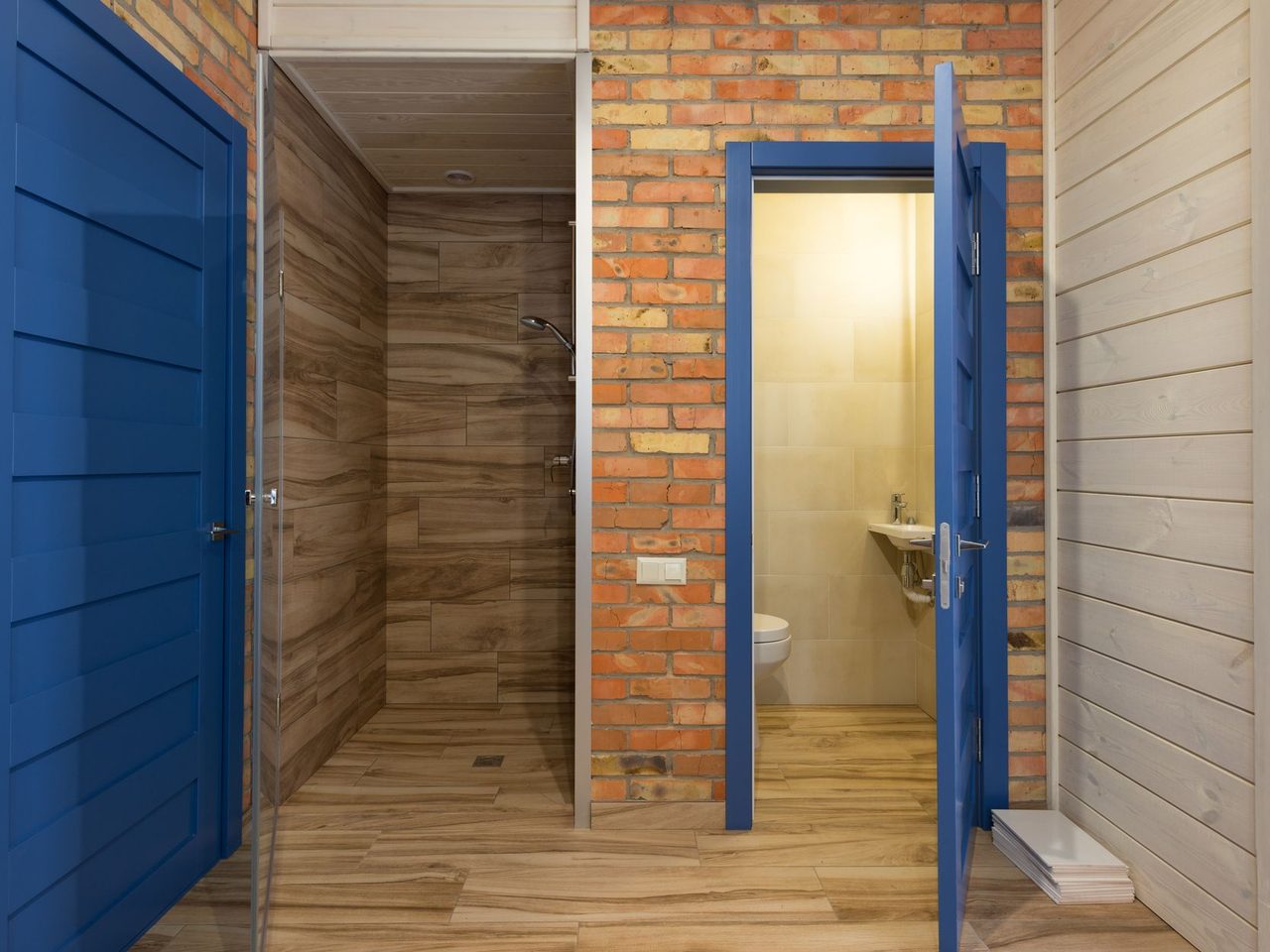 Bathroom with brick and wood walls, blue doors and a wood-look floor