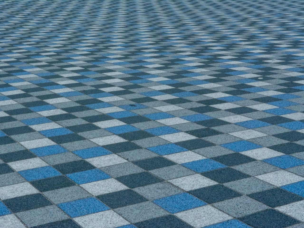 Low-angle view of a large floor covered in blue, gray and light gray square carpet tiles arranged in a checkered pattern