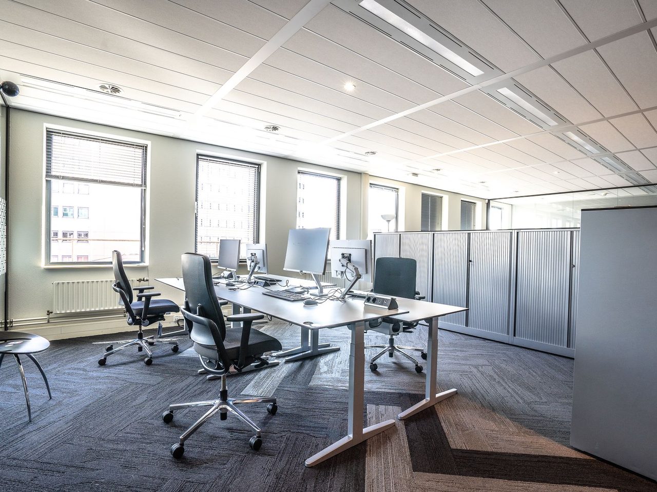 Open office with workstations and ergonomic chairs on gray carpet tile