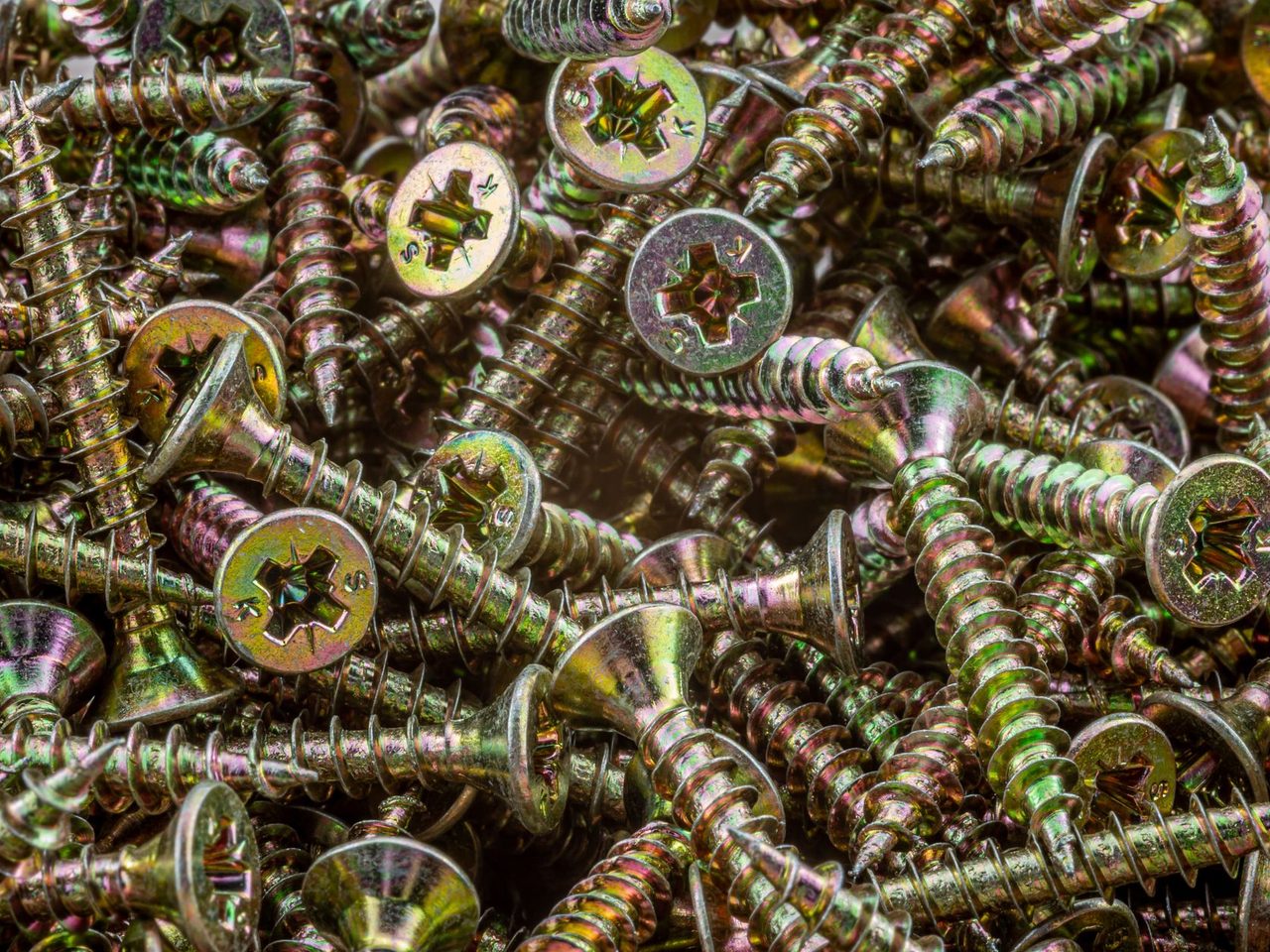Close-up of many gold-colored metal screws with countersunk cross-recess heads and coarse threads piled together in a heap.