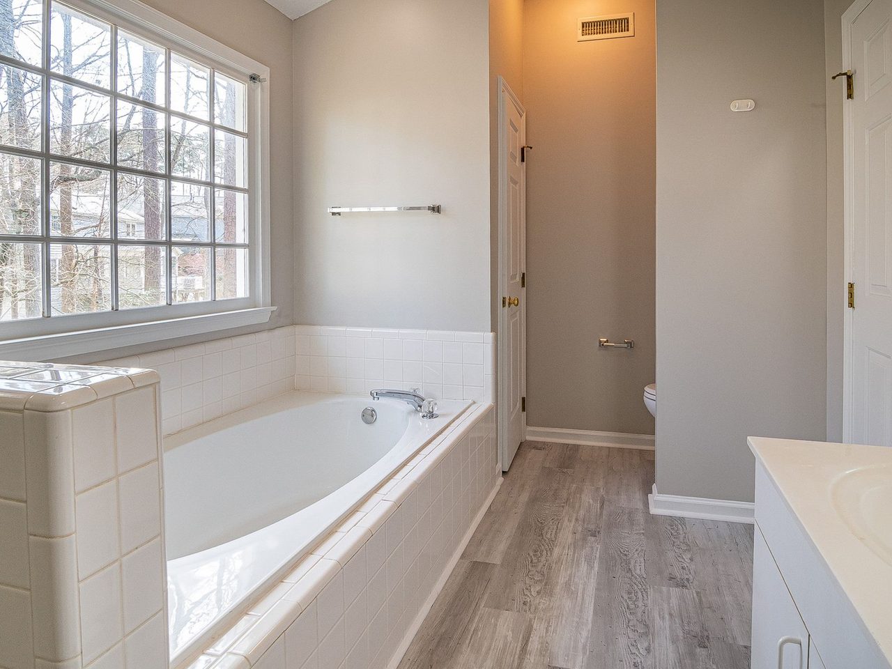 Bathroom with a built-in bathtub beside a gray wood-look plank floor and a large window