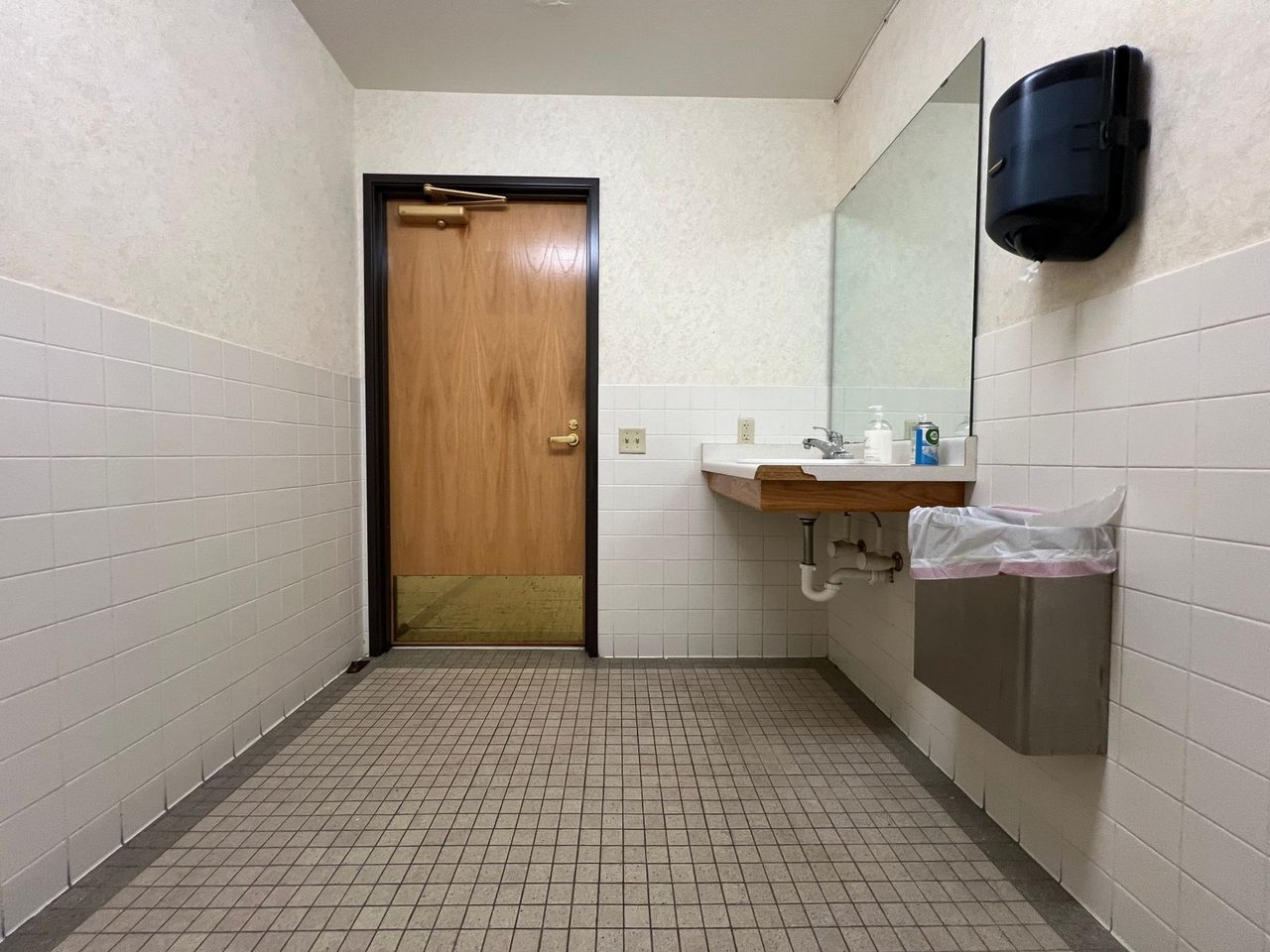Public restroom with a small-tile floor, a wall-hung handbasin and a wooden door