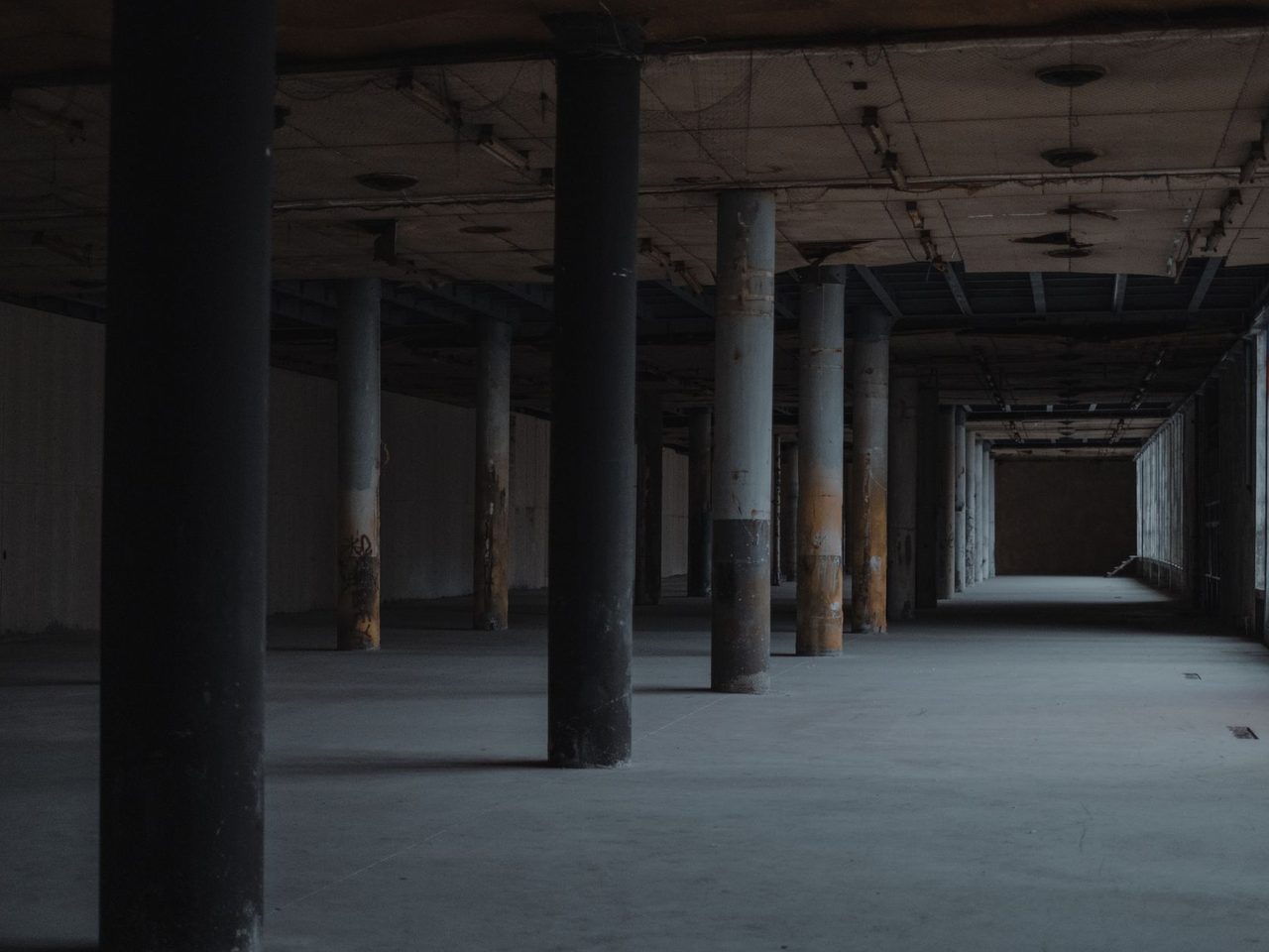 Empty hall with rows of columns and a bare floor leading to far windows
