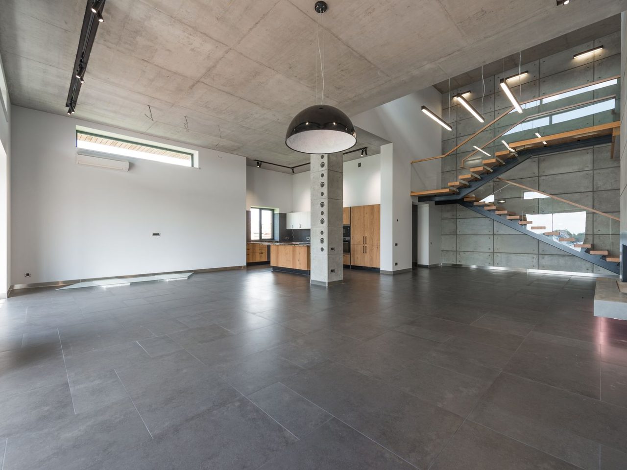 Open-plan interior with a gray stone floor, a column and a staircase