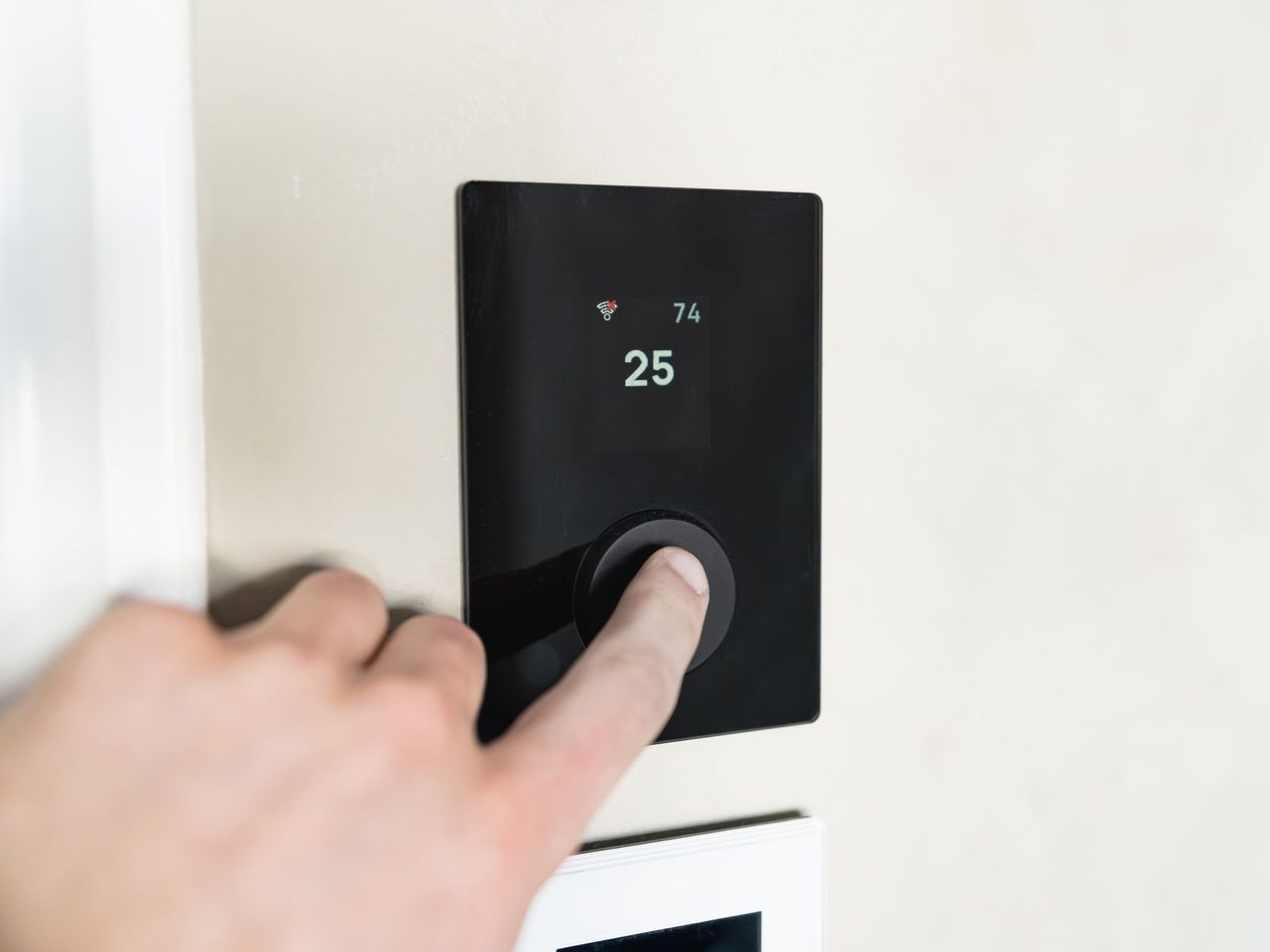 Hand adjusting a modern wall-mounted thermostat