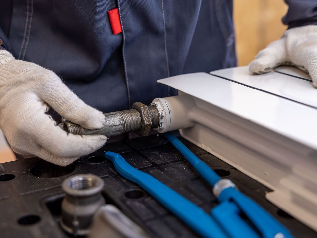 Gloved hands fitting a heating pipe with tools