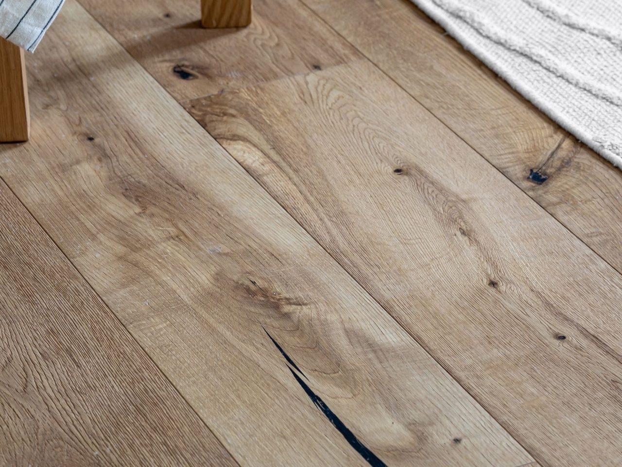 Wood plank floor with a dark split across one plank beside a woven rug