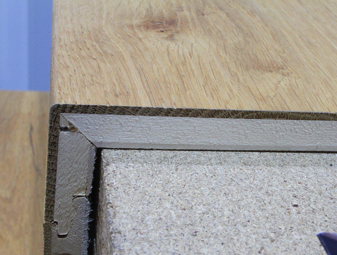 Cut end of a wood-look stair element showing the oak surface layer and particleboard core