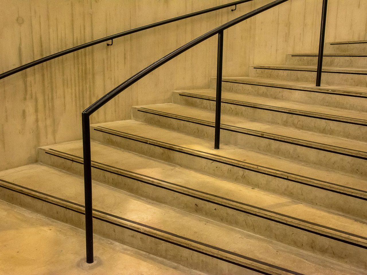 Close-up of an indoor concrete staircase with black handrails