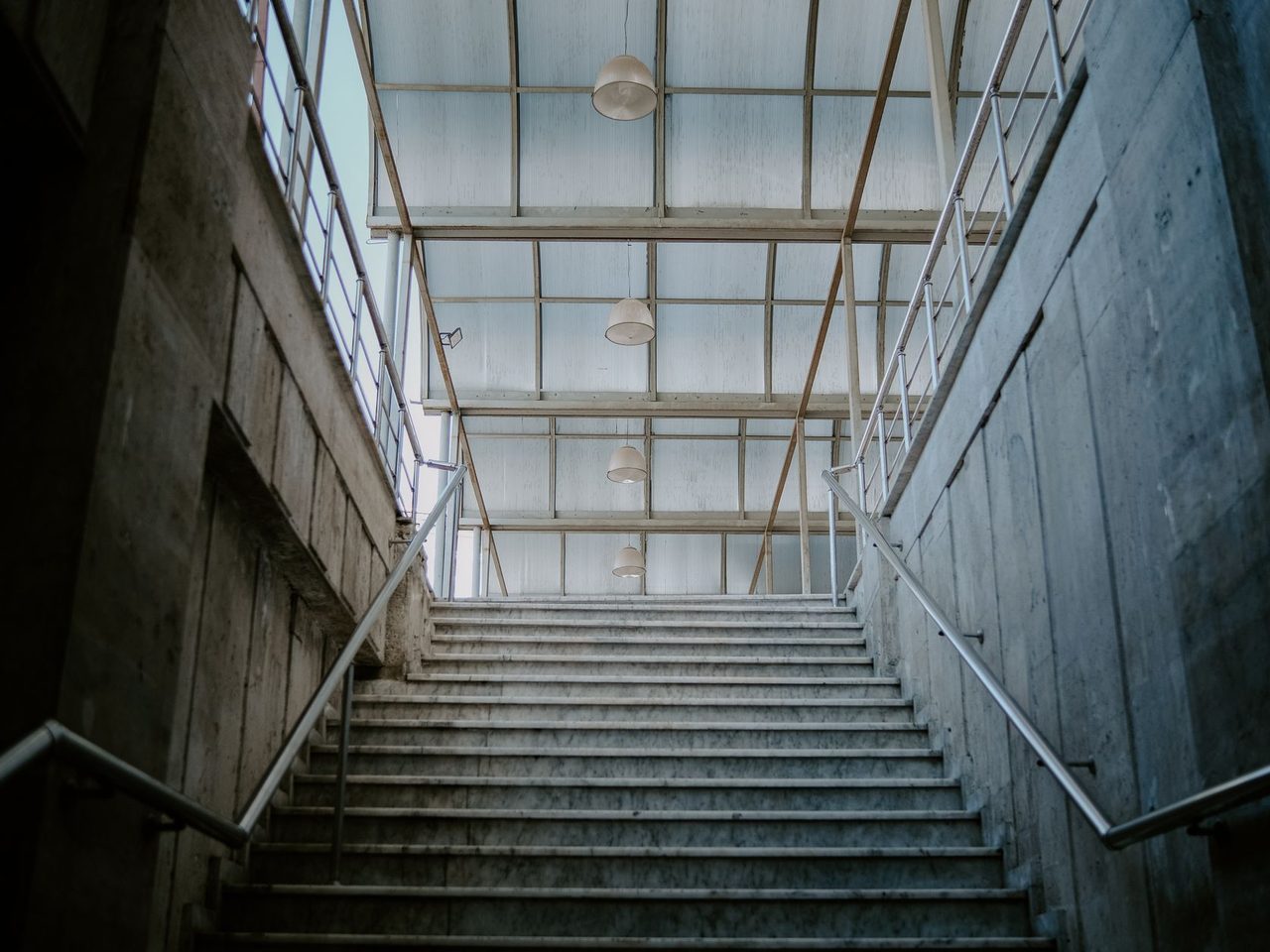 Indoor concrete staircase with metal railings rising under a glass roof