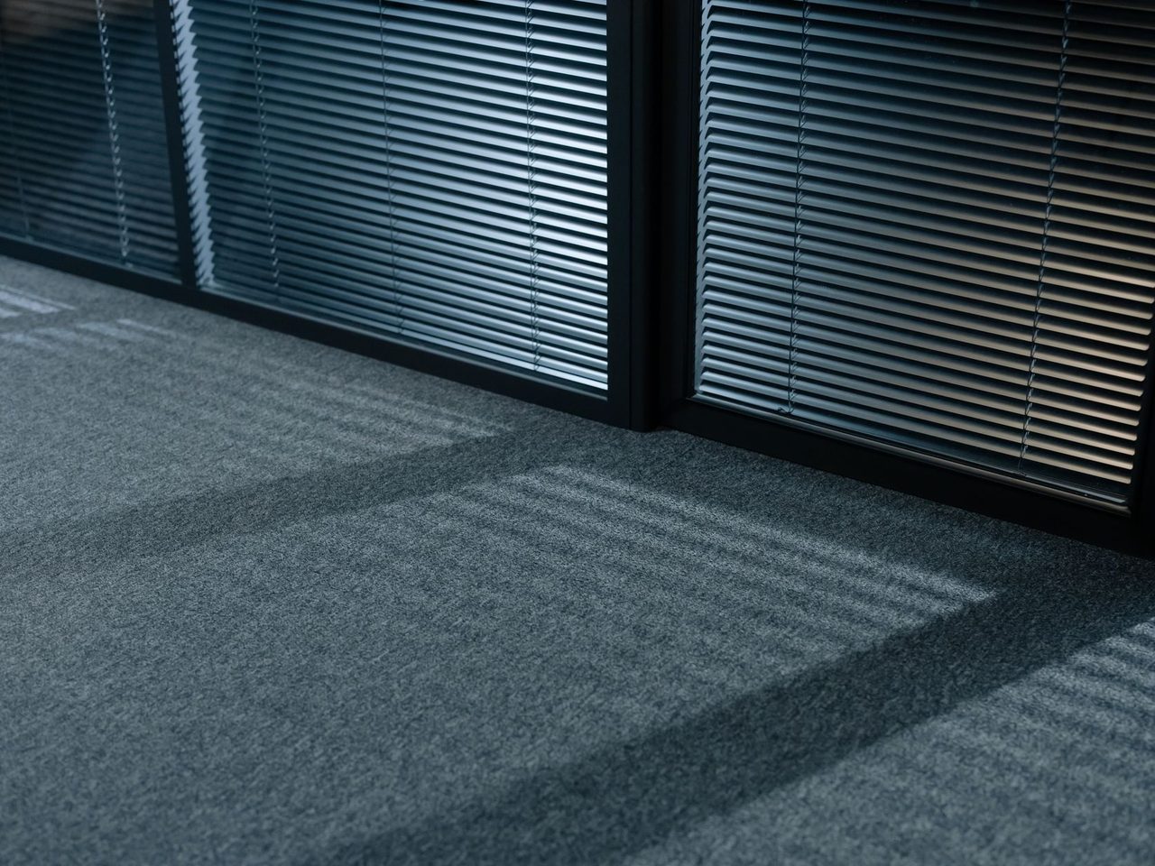 Shadows from venetian blinds falling across a gray carpeted floor