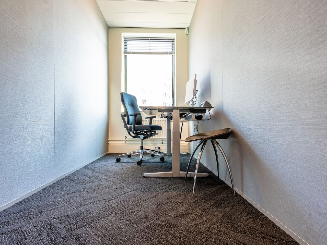 Small office with a desk and chair on dark carpet by a window