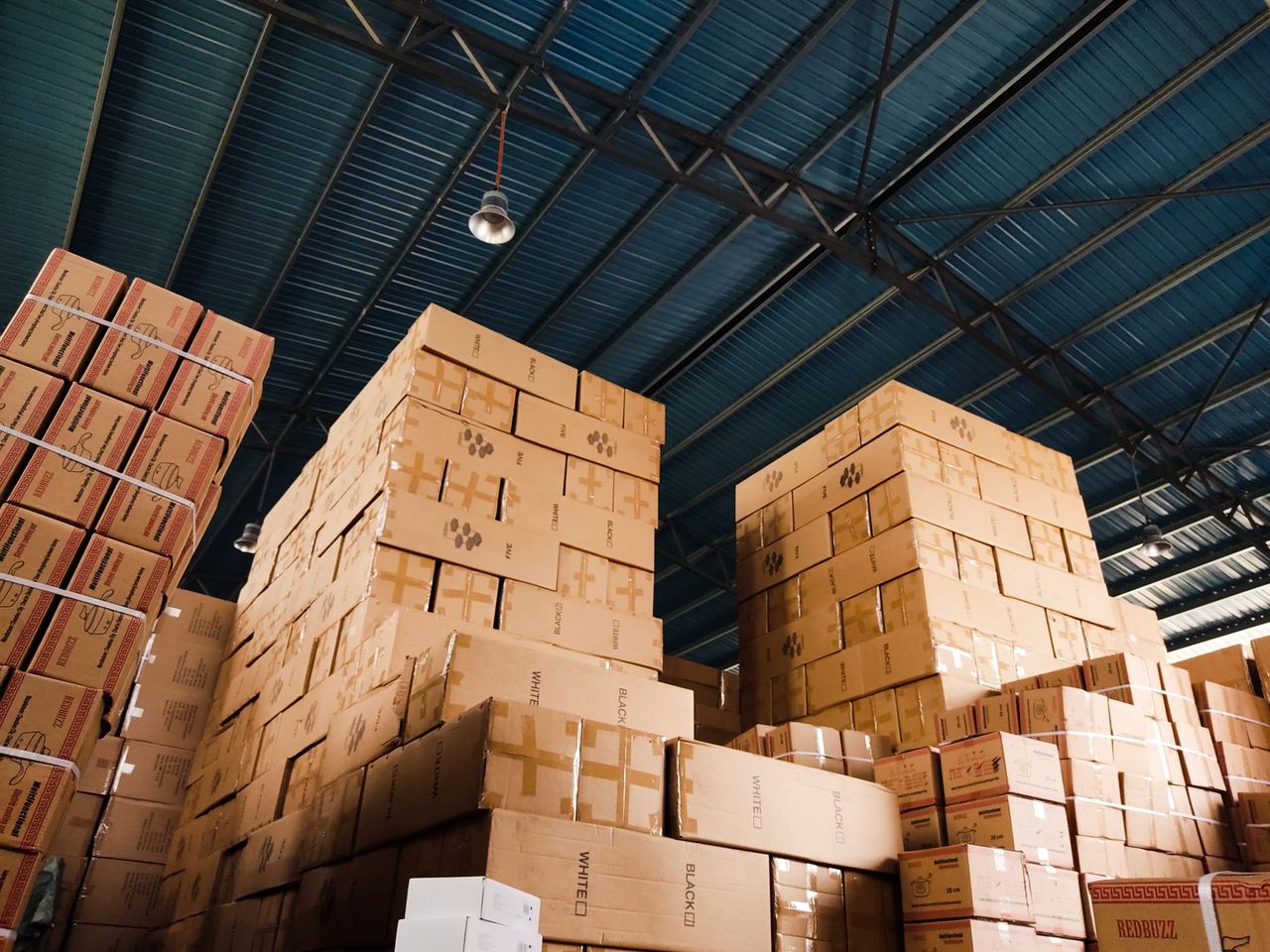 High stacks of cardboard cartons in a warehouse under a blue metal roof