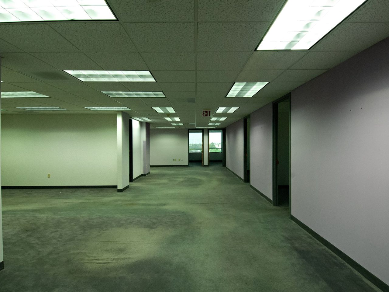 Empty office floor with green carpet under fluorescent lights