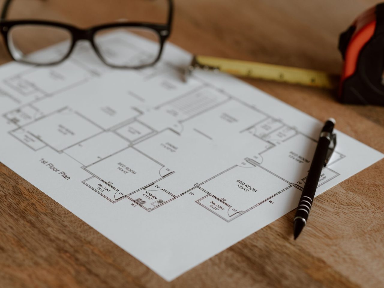 House floor plan on a wooden desk with a pencil, ruler and glasses