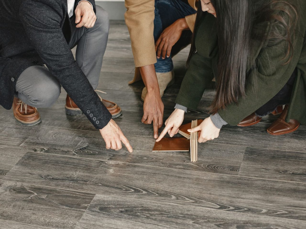 Hands of several people pointing at wood flooring samples laid on a floor