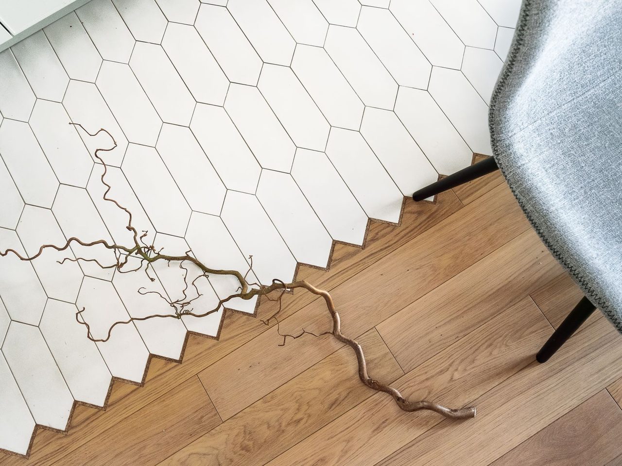 Overhead view of a wood floor meeting white hexagonal tile along a zigzag edge