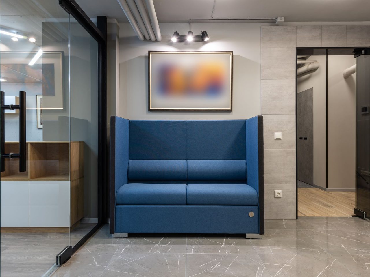 Office lounge with a blue sofa on a tile floor beside glass partitions