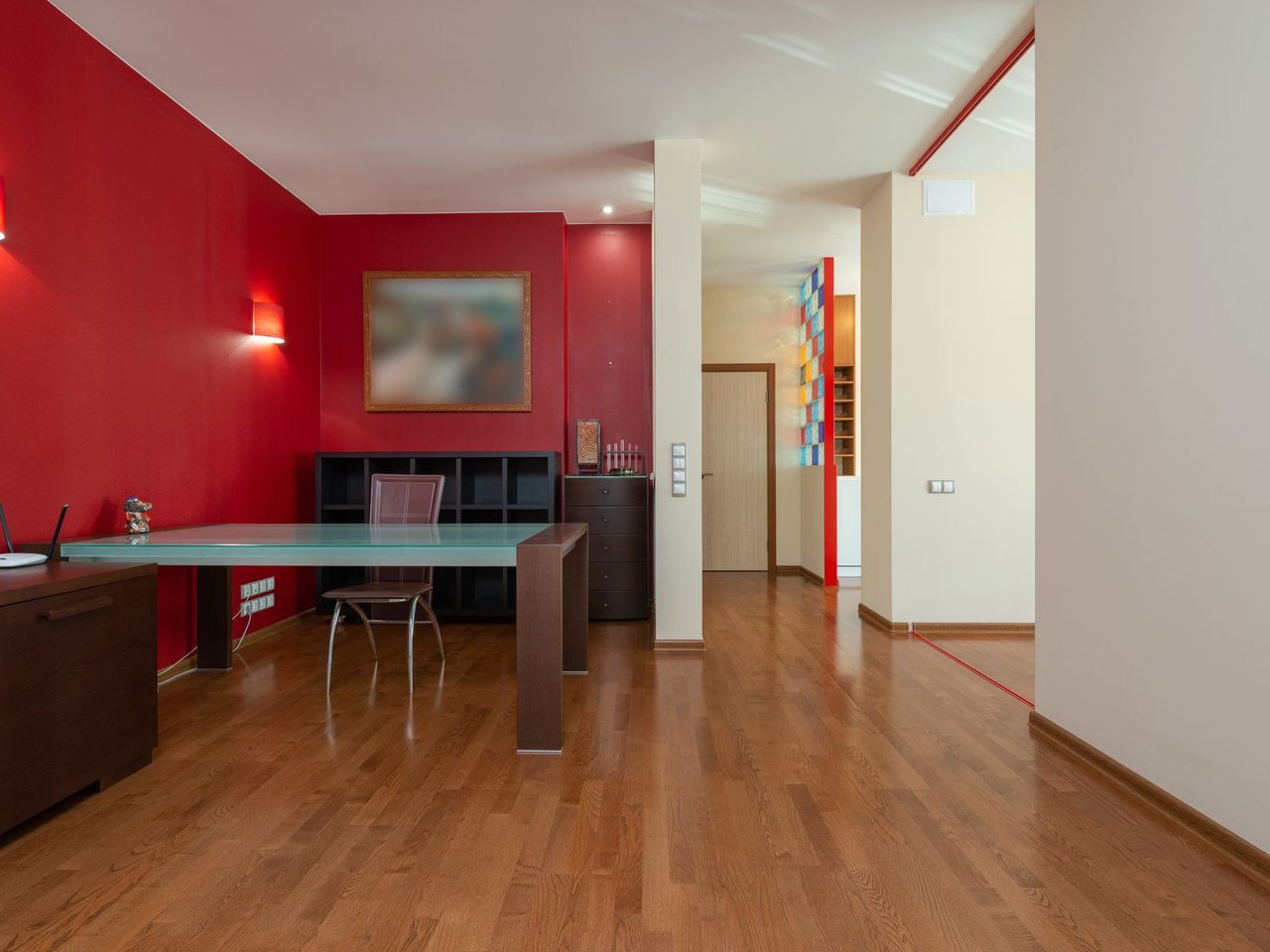 Interior with a desk, a red wall and several doorways off a wood floor