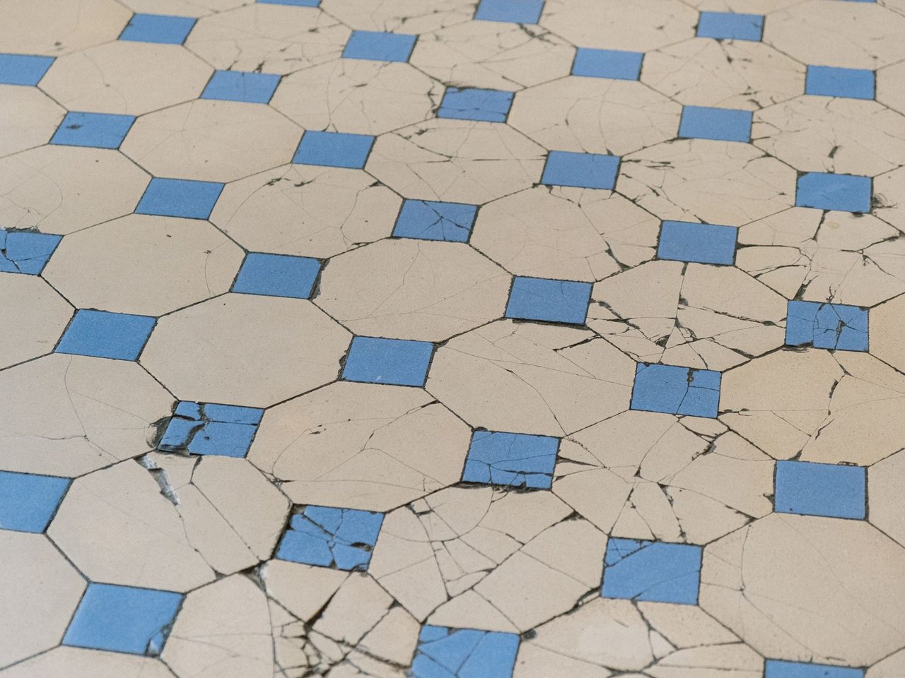 Aged floor tiles in a blue and white geometric pattern with many cracks