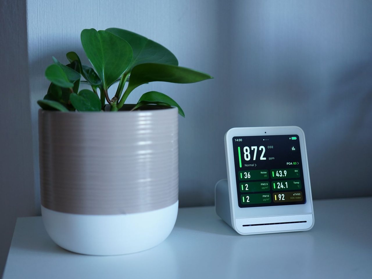 Indoor air quality monitor showing CO2 readings beside a potted plant