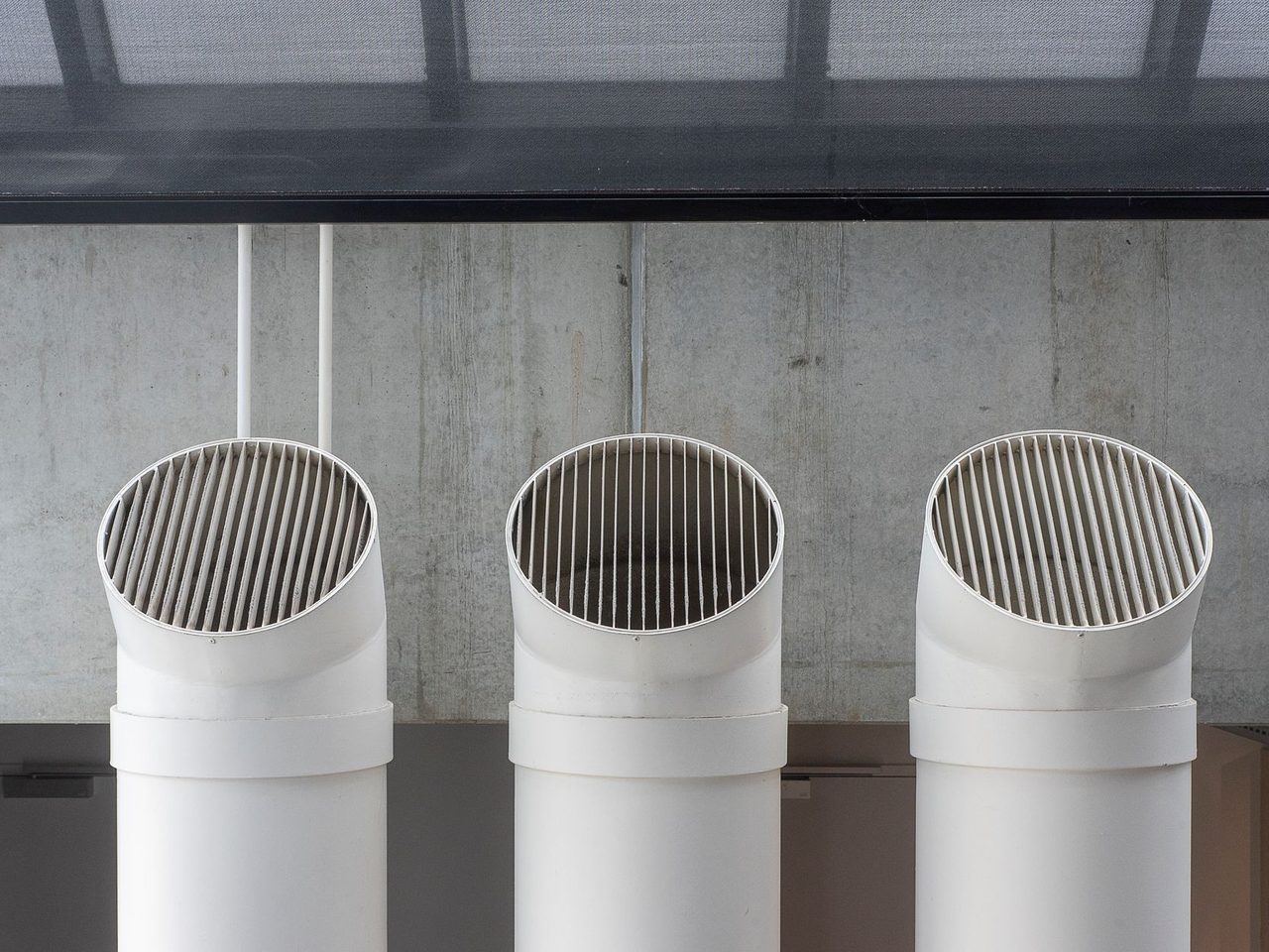 Three white ventilation ducts on a concrete wall