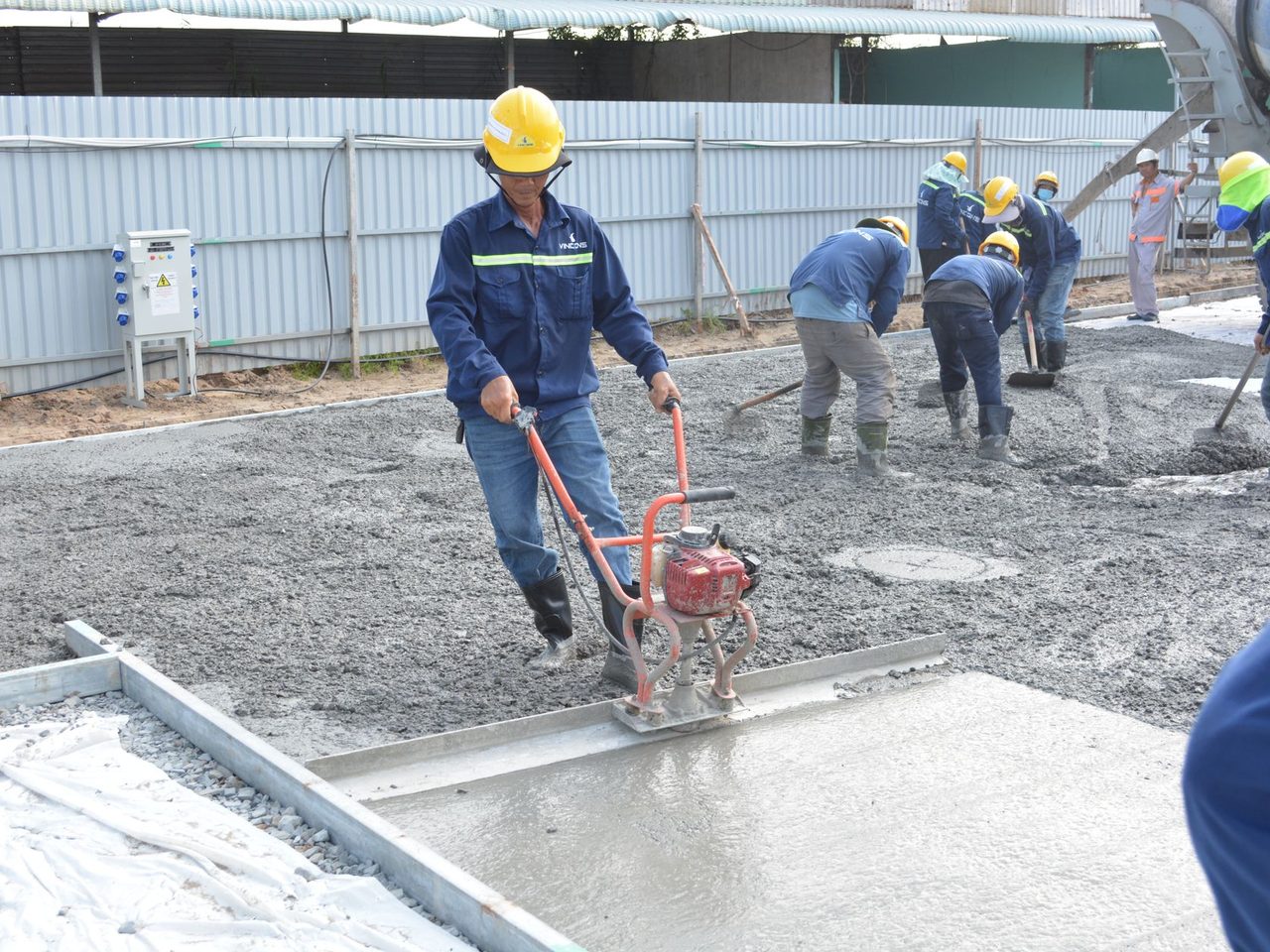 Crew in safety gear smoothing and leveling a wet concrete floor