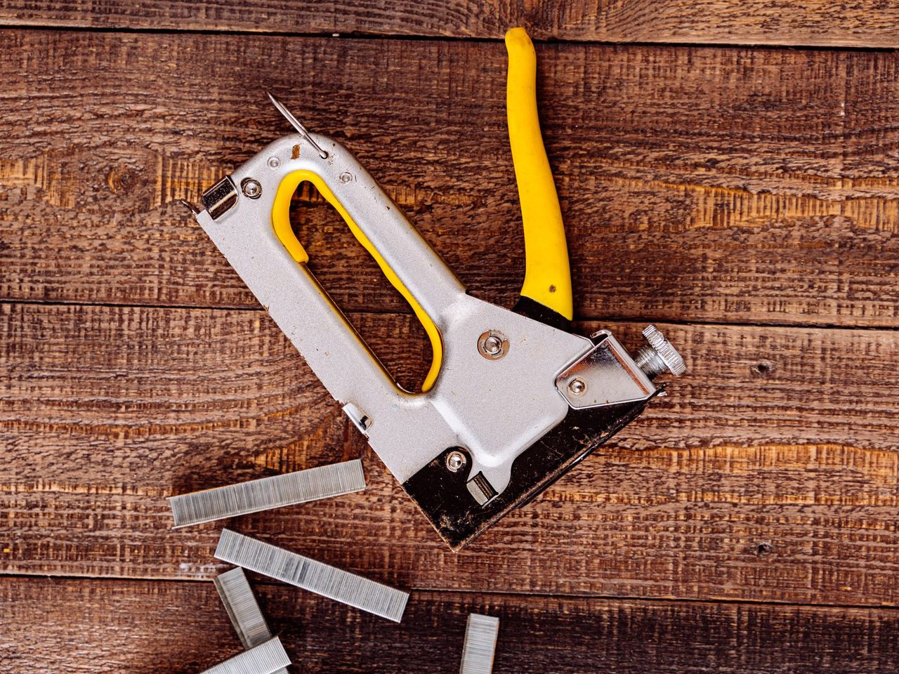 Staple gun with a yellow handle and loose staples on a wooden surface