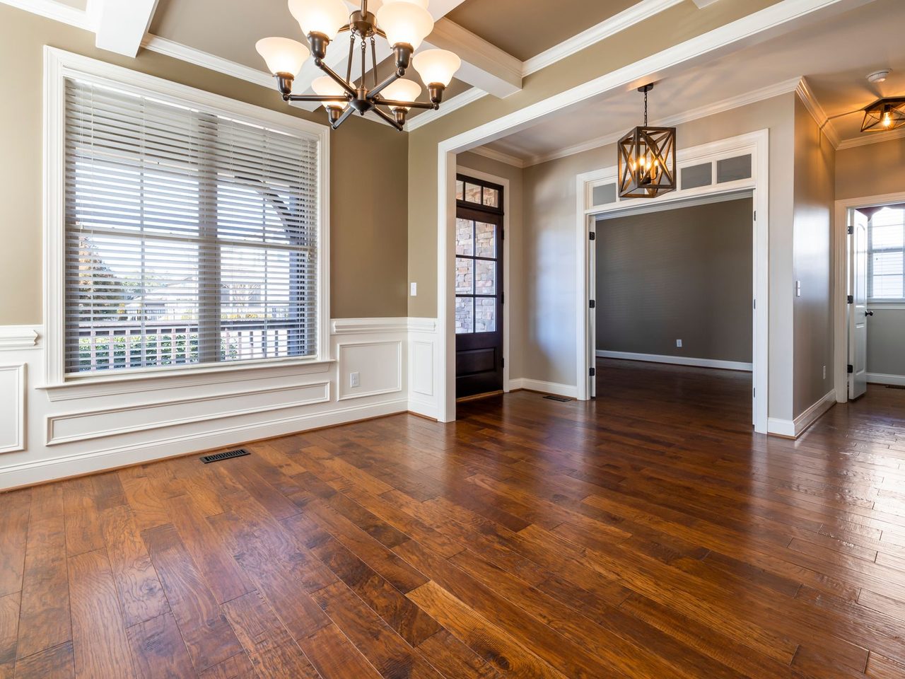 Room with a dark hardwood floor, chandeliers and wainscoting