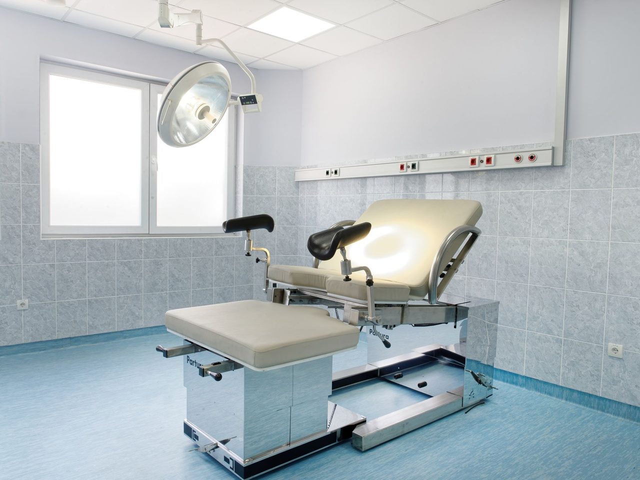 Examination room with an adjustable chair, a blue floor and tiled walls