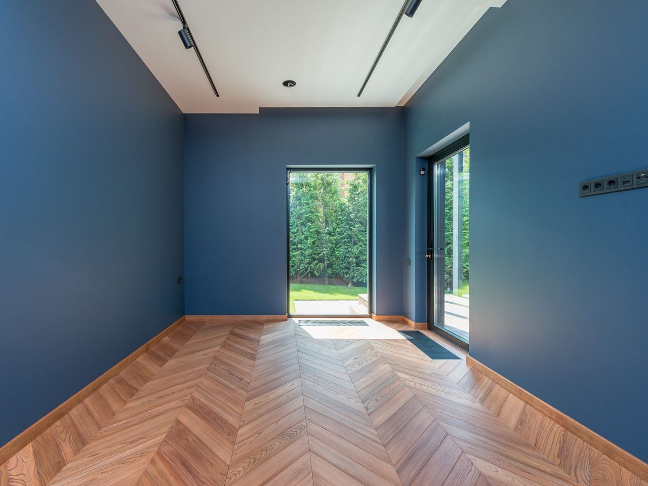 Room with blue walls and a light herringbone floor running toward glass doors
