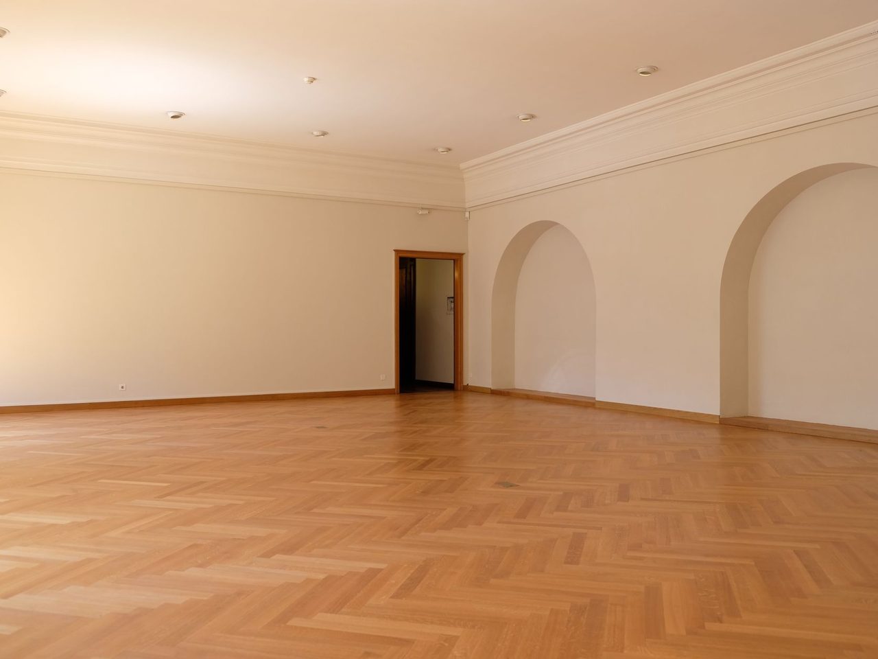 Large empty room with a honey-toned herringbone floor and arched openings