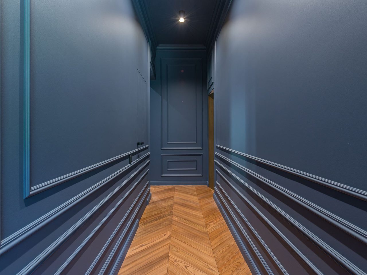 Corridor with a chevron-patterned wood floor between dark blue walls