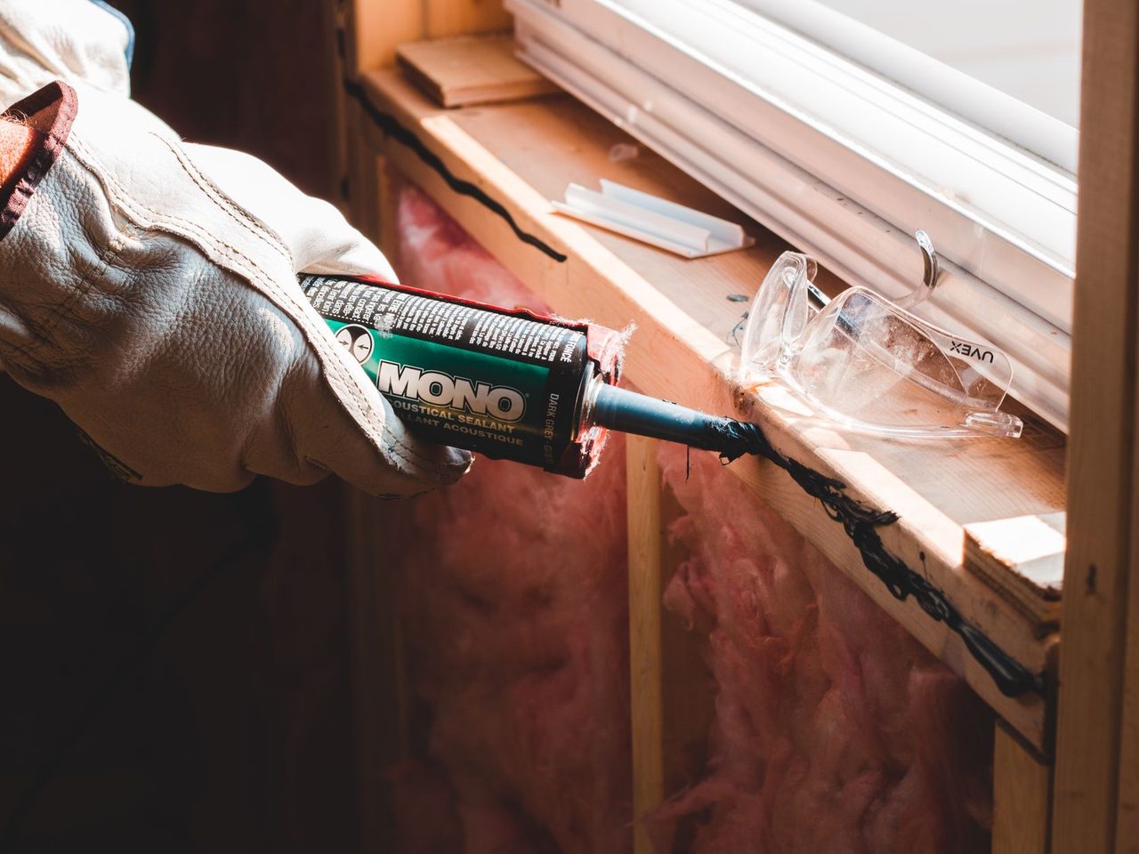 Gloved worker applying a bead of sealant from a cartridge gun