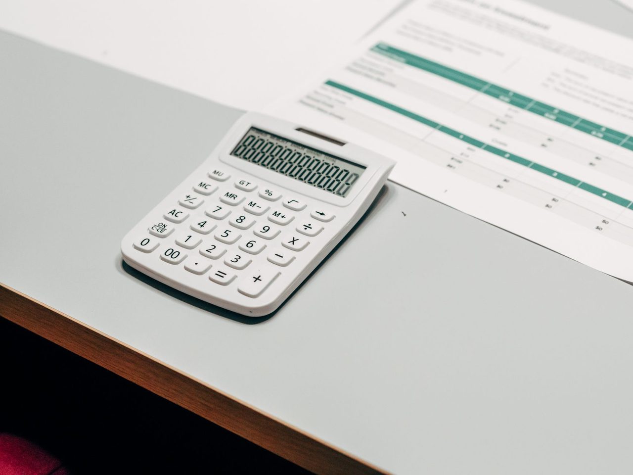 White calculator beside a printed spreadsheet on a desk