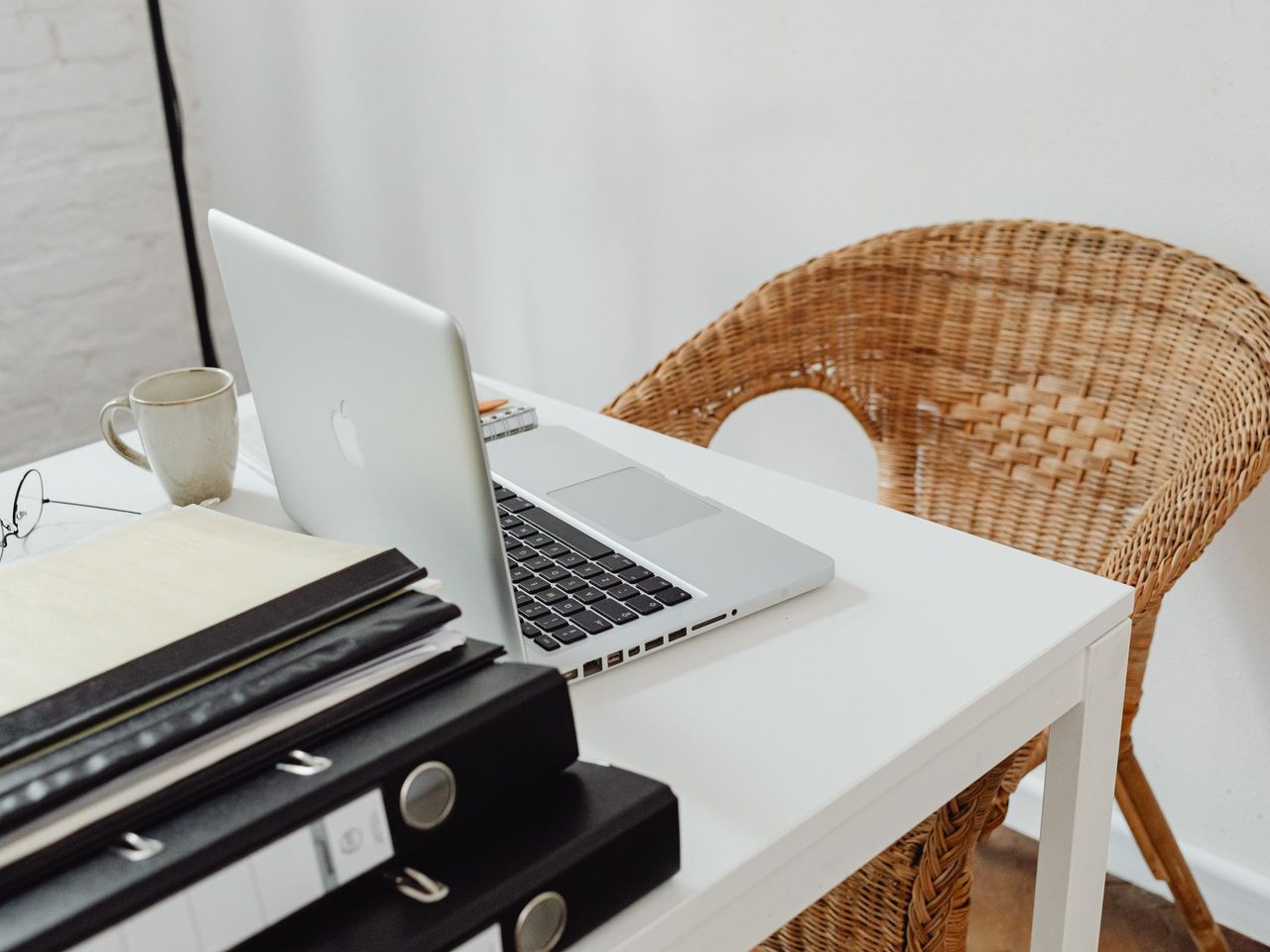 Home office desk with a laptop, binders and a wicker chair