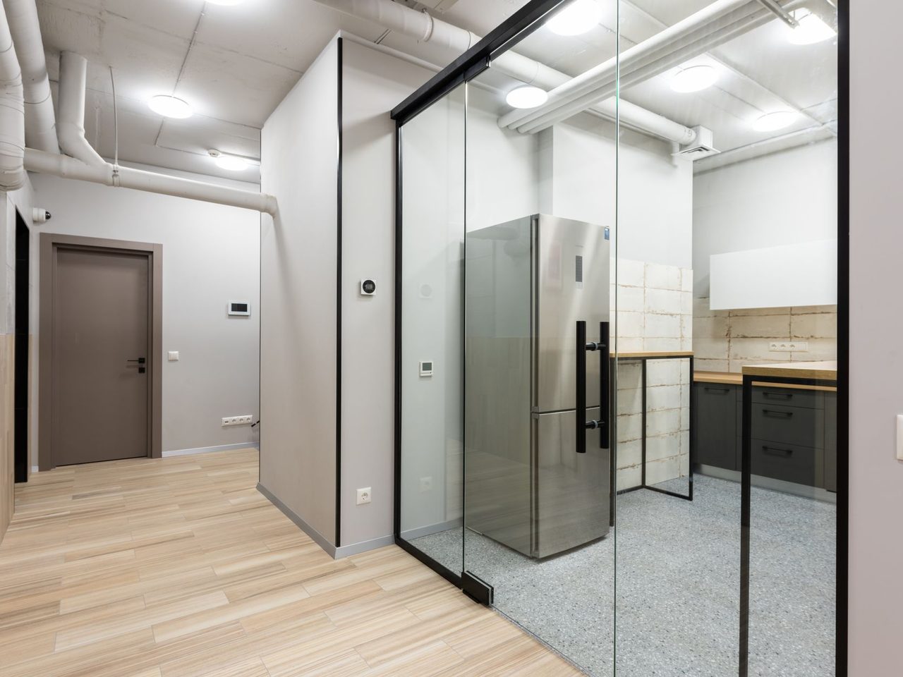 Workplace hallway and kitchen with glass walls and a light wood-look floor