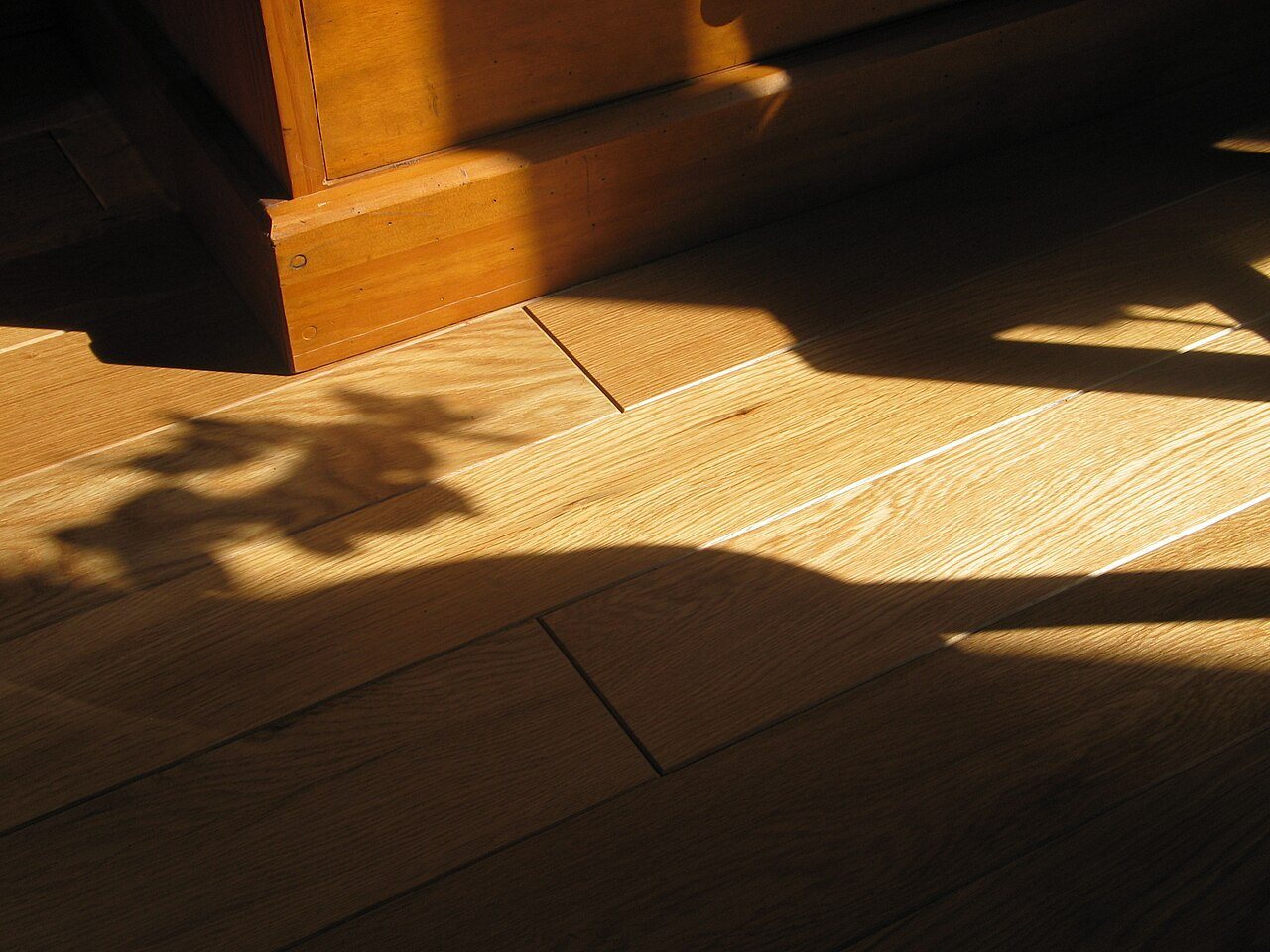 Close-up of solid oak floorboards with bevelled edges in low sunlight beside a cabinet base