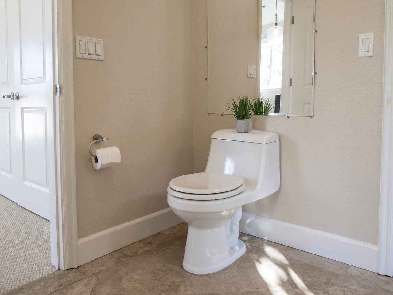 Toilet on a light bathroom floor next to a white baseboard and an open door