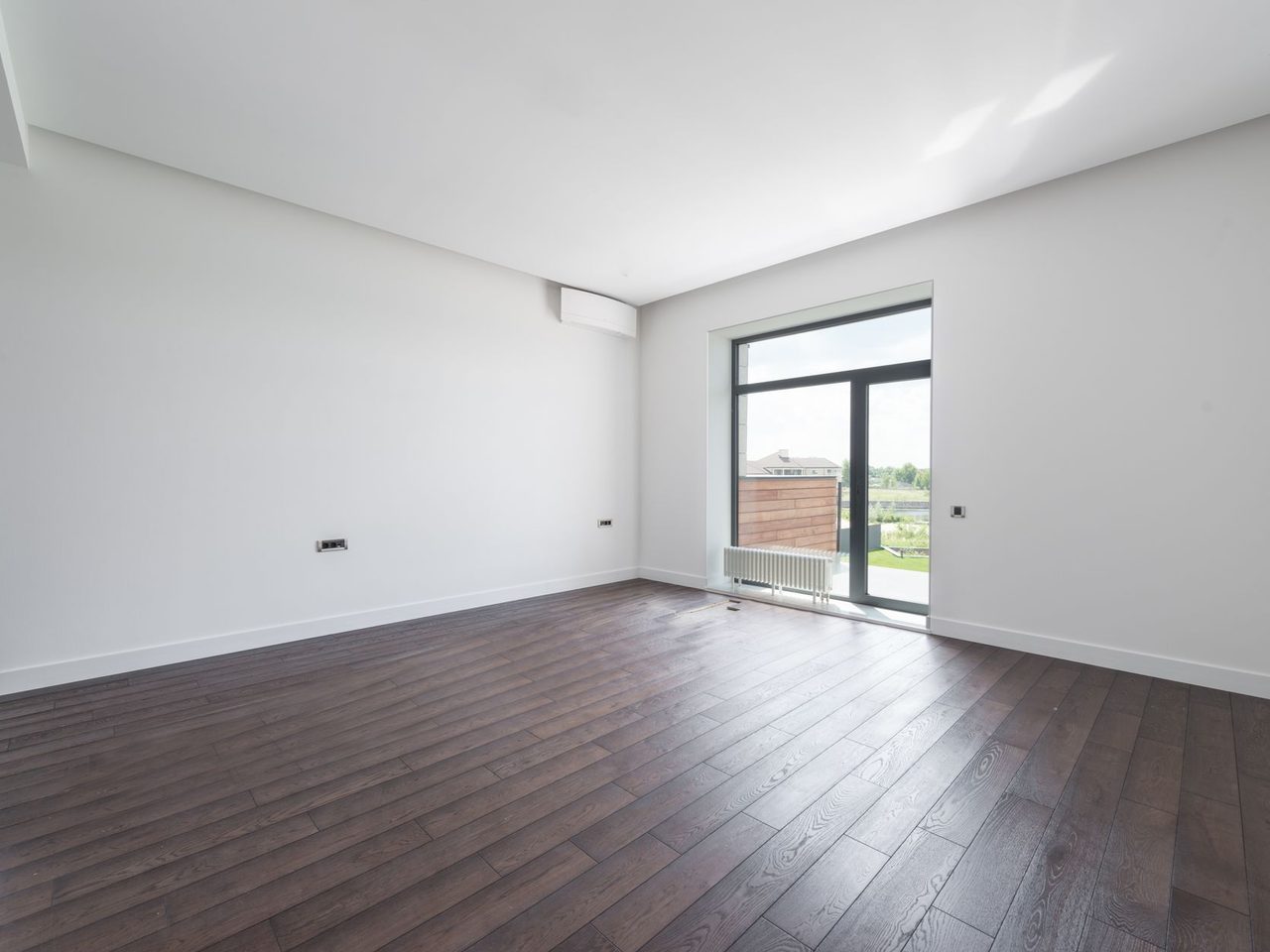 Empty room with a dark plank floor and a large sunlit window