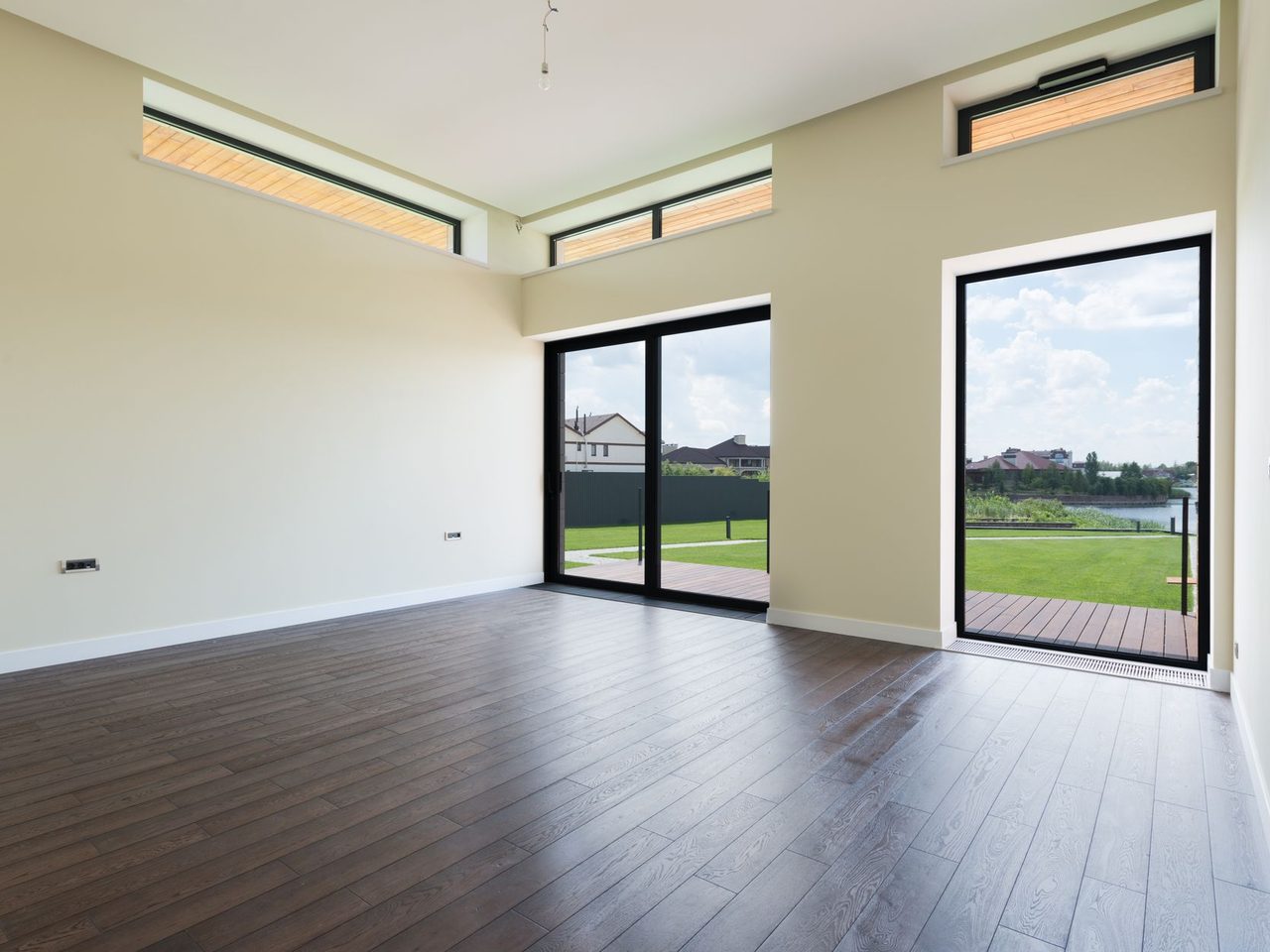 Empty room with tall glass doors to a terrace and a dark plank floor
