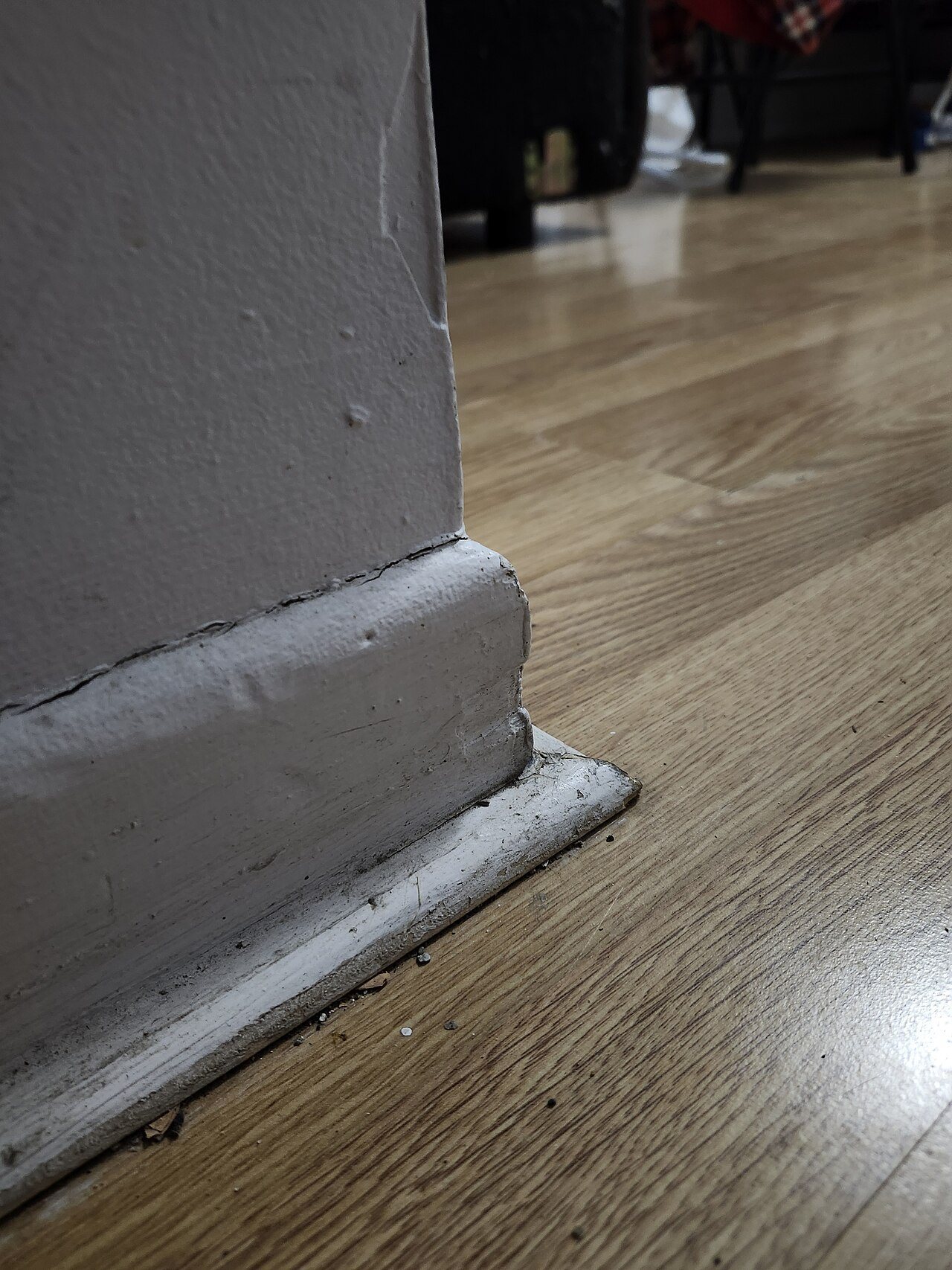 Painted baseboard and shoe strip at an outside wall corner over a wood-look plank floor