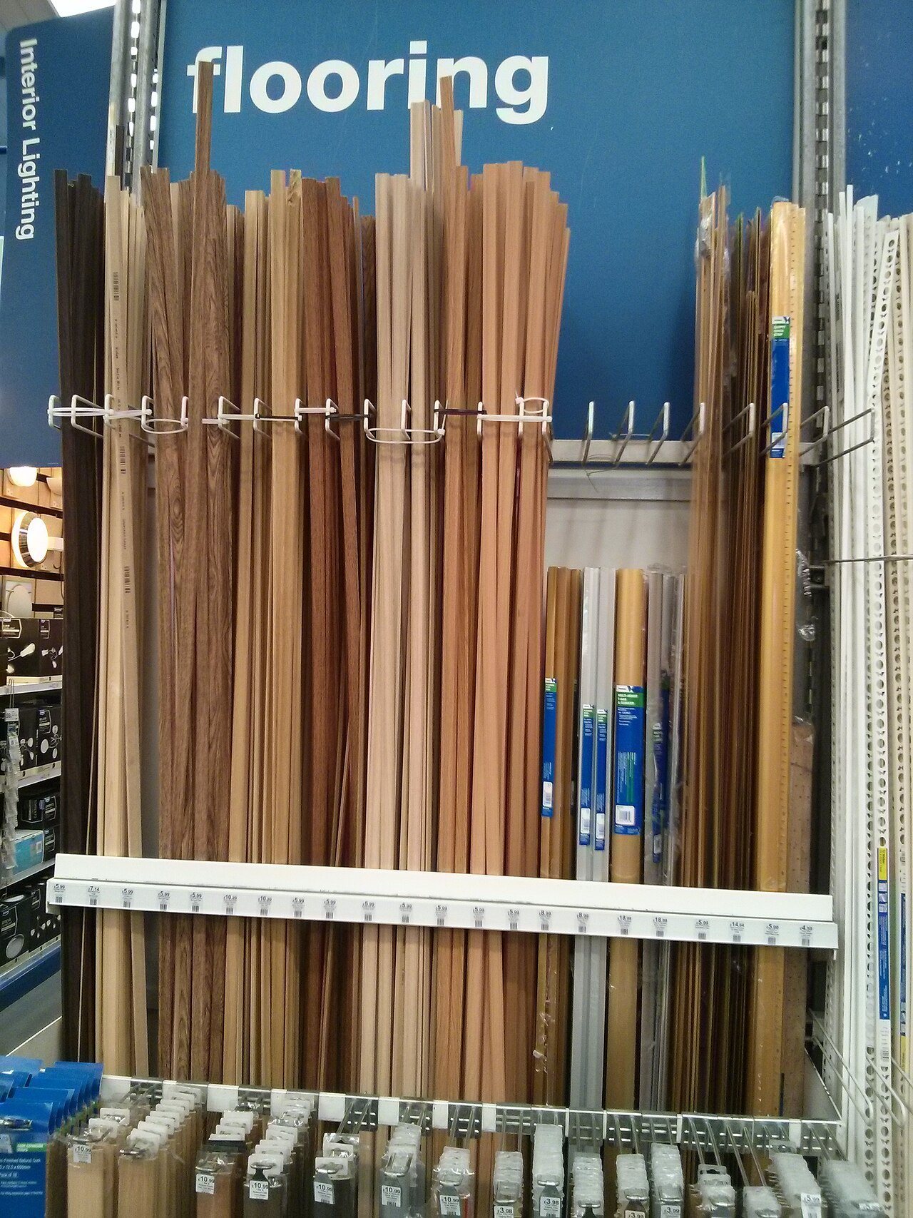 Store rack of wood-look and metal flooring transition strips and moldings under a flooring sign