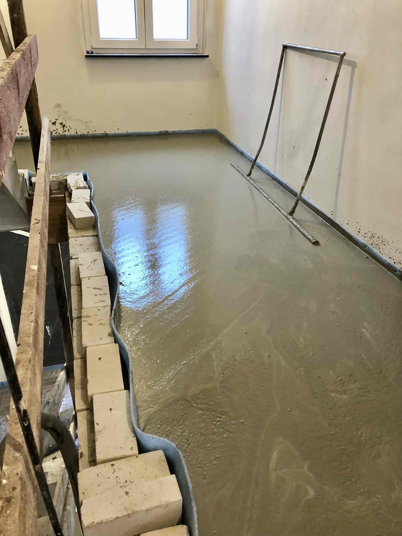 Freshly poured floating screed with a wet sheen across an empty room under renovation